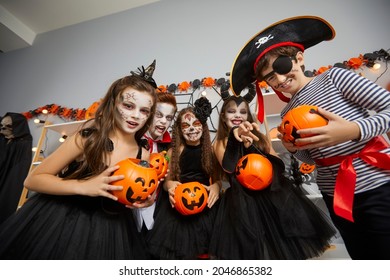 Little boys and girls disguised as various spooky characters want tricks or treats at Halloween party. Kids hold pumpkin-shaped bucket for Halloween or lantern and look into camera in frightening way.