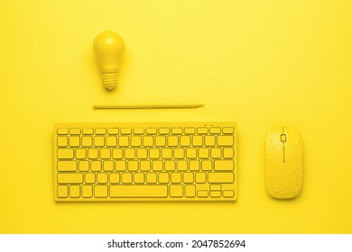 Papan ketik kuning dengan tetikus, pensil, dan bola lampu di latar belakang kuning. Konsep bisnis dan minimalis. Satu warna.