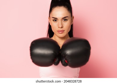 young strong woman in sportswear and blurred boxing gloves on pink
