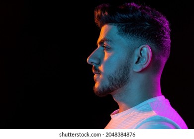Profile view. Latino young man's portrait on black studio background in neon light. Handsome male model. Concept of human emotions, facial expression, youth, sales. Copy space for ad.