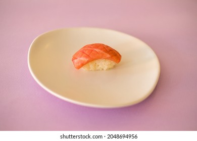 Sushi Nigiri with raw tuna served on white plate. One sushi piece on the white plate isolated on pink background. Japanese traditional food. 