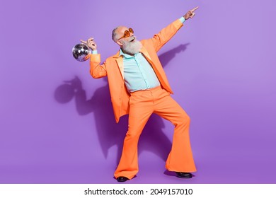 Volledige foto van een oude positieve gelukkige man die een discobalpunt vasthoudt en een lege ruimte ziet geïsoleerd op een paarse kleurachtergrond
