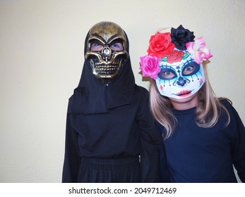 Children dressed in black costumes and scary Halloween masks. Girl in a Mexican Kalaka Calavera mask. A boy wearing a horrible skull mask with a black hood. All Hallows Eve or All Saints Eve theme.