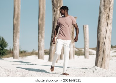 陽気な笑顔のスタイリッシュなアフリカ、ピンクの t シャツと白いズボンの男、アフリカ系アメリカ人のモデルの男、乾燥した砂漠を歩く、ファッション コンセプト、人々、野生の西スタイル