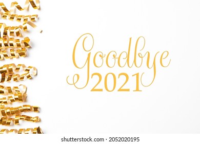 Serpentinas doradas brillantes y frase Adiós 2021 sobre fondo blanco, vista superior