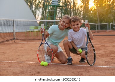 Niños lindos con raquetas de tenis y pelotas en la cancha al aire libre