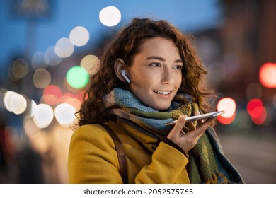 Gelukkige vrouw die bericht opneemt met behulp van stem op smartphone. Gelukkige vrouw die 's avonds audio op mobiele telefoon op straat opneemt. Glimlachende vrouw die op haar slimme telefoon in de winteravond spreekt.