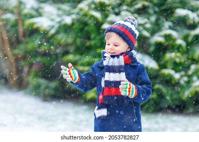 Schattig klein grappig kind in kleurrijke wintermode die plezier heeft en met sneeuw speelt, buiten tijdens sneeuwval. Actieve vrijetijdsbesteding in de buitenlucht met kinderen. Kid jongen en peuter sneeuwvlokken vangen.