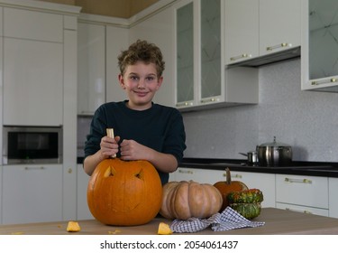 Een gelukkige 11-jarige tiener met een Europees uiterlijk bereidt zich voor op de Halloween-vakantie en snijdt thuis in een witte keuken een grote oranje pompoen met een mes. Voorbereiding voor de Halloween-vakantie