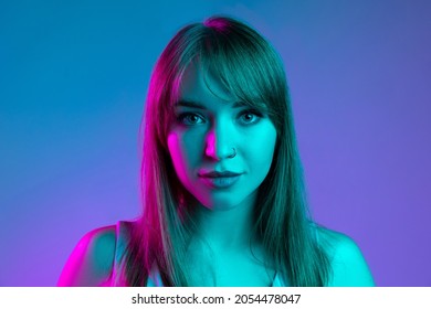 Potret close-up gadis cantik muda yang terisolasi dengan latar belakang studio biru dalam filter cahaya neon. Konsep emosi manusia, ekspresi wajah, masa muda, penjualan. Terlihat tenang, sedih, serius. Salin ruang untuk