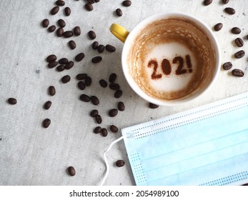 Adiós 2021 y COVID-19, un año que muchos quieren que el tiempo pase volando. Taza de café con el tema del arte de la comida navideña con el número 2021 en la parte inferior de la taza sobre fondo de cemento con máscara médica desechable y granos de café.