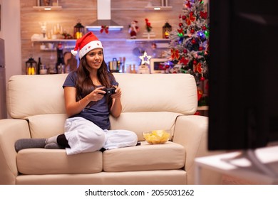 Meisje met gaming-joystick die online videogame speelt tijdens virtuele competitie die geniet van de wintervakantie in een met kerst versierde keuken. Vrouw viert kerstseizoen thuis