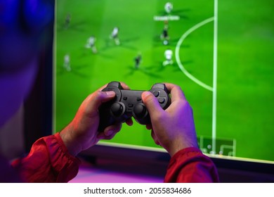 Vista posteriore del giovane giocatore video computer pc. Giovane uomo seduto su una sedia nella postazione di gioco che tiene in mano un joystick. Streamer uomo che indossa cuffie che gioca a calcio online nella camera oscura.