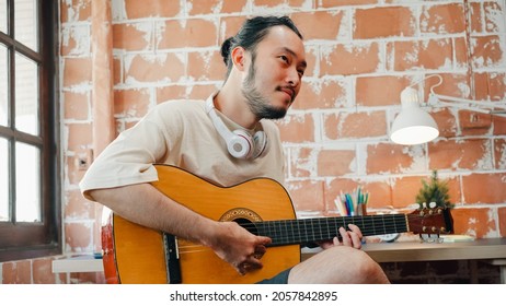 Artistes produisant de la musique dans leur studio d'enregistrement à domicile, homme asiatique jouant de la guitare et chantant dans le salon à la maison. Concept de style de vie d'un homme se détendant le matin à la maison.