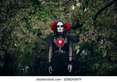 Tânără cu machiaj cu craniu de zahăr și trandafiri roșii, îmbrăcată în costum negru al morții, în timp ce Santa Muerte este pe fundalul pădurii. Conceptul Ziua Morților sau Halloween.
