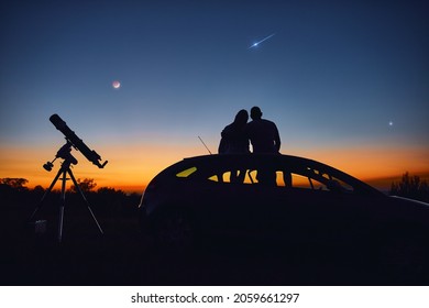 Pareja mirando las estrellas junto con un telescopio astronómico.