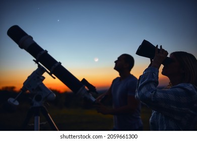 Pareja mirando las estrellas junto con un telescopio astronómico.