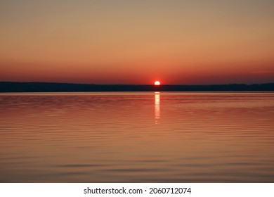 Majestueus uitzicht op de zonsondergang - de zon gaat onder achter een berg met de zee op de voorgrond. Er vliegen wat vogels ver weg op de achtergrond. De zon schiet wat zonnestralen uit.