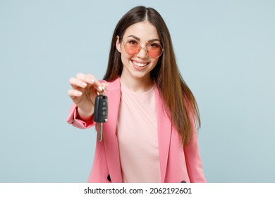 Junge Spaß glücklich lächelnde erfolgreiche kaukasische Frau der 20er Jahre, die eine pastellrosa Kleidungsbrille trägt, die das schlüssellose System des Autoschlüssels verschenkt, das auf blauem Hintergrundstudio isoliert ist. People-Lifestyle-Konzept.