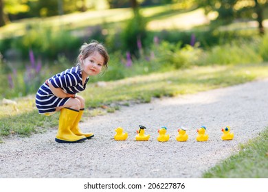 Schattig klein meisje van 2 spelen met gele rubberen eenden in zomerpark.