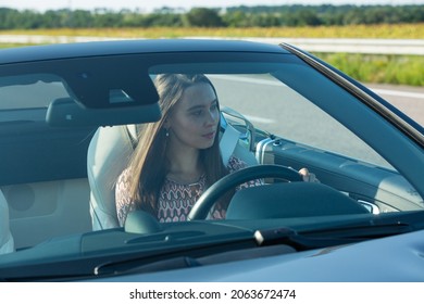 Mooie jonge vrouw een Mercedes Benz SL550 cabrio rijden op de weg. Het meisje is zeer attent en gefocust tijdens het rijden.