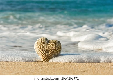Piedra en forma de corazón con corales en el interior bañados por un océano azul profundo en una playa de arena con espuma blanca alrededor
