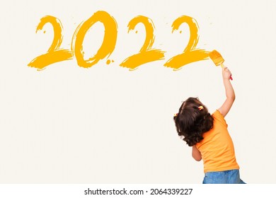Niedliches kleines Mädchen zeichnet das neue Jahr 2022 mit Pinsel auf Wandhintergrund