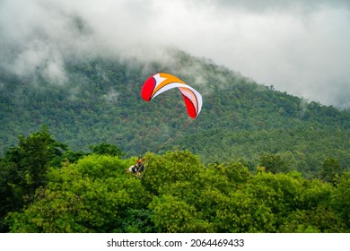 El deportista en un paramotor deslizándose y volando en el aire con nubes majestuosas y bosque verde son el fondo. El paramotor es un deporte extremo.