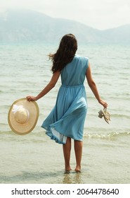 Hình ảnh một người phụ nữ trẻ tóc nâu mặc váy xanh đi chân trần trên bãi biển và đung đưa chân trong nước. Người phụ nữ trẻ trong bộ váy trắng mùa hè với chiếc mũ rơm nhìn lên bầu trời và biển cả. Xem lại.