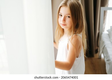 Porträt eines achtjährigen Schulmädchens mit blonden blonden Haaren am Morgen am Fenster