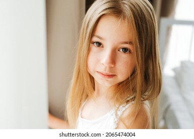 Porträt eines achtjährigen Schulmädchens mit blonden blonden Haaren am Morgen am Fenster