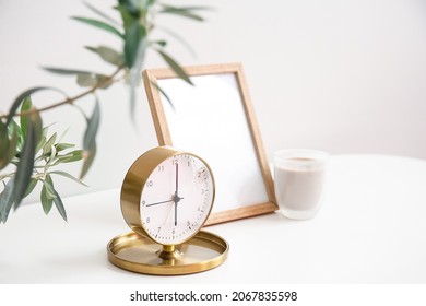 明るい壁の近くのテーブルにスタイリッシュな目覚まし時計とキャンドルを置いた空白のフレーム