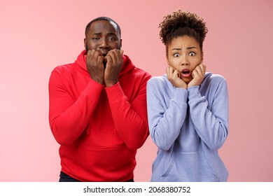 震惊害​​怕两个没有安全感的年轻非裔美国夫妇都吓坏了蜘蛛站在床上吓得僵住了手牵着嘴咬手指颤抖恐惧，粉红色背景
