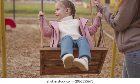 ブランコに乗って笑いながら飛び上がる小さな子供、秋の遊び場、幸せな家族、都市公園で子供を転がす母親、空を飛ぶ子供の頃の夢、散歩中のお母さんに微笑む、赤ちゃんと遊ぶ