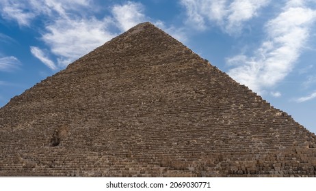 De Grote Piramide van Cheops op de achtergrond van een blauwe lucht met pittoreske wolken. Aan de muur, gemaakt van oude rotsblokken, zie je de ingang naar binnen. Egypte. Gizeh