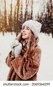 Mooie jonge vrouw in besneeuwde mooie winter bos. Meisje draagt ​​pluizige handschoenen, pet en jas. Winterbos, bomen op onscherpe achtergrond. Gekruiste handen vanwege koud weer. Hoge kwaliteit foto