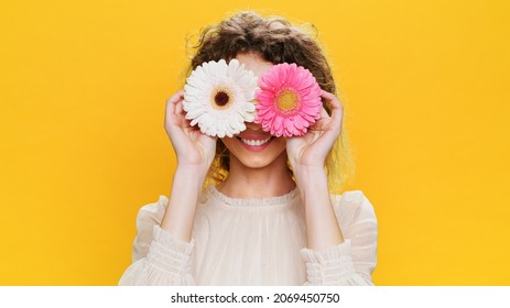 Mujer joven feliz sonriendo flores rosadas cerca de sus ojos abre la cara saca la lengua sobre fondo amarillo. Retrato de personas con emociones positivas de Glamorous, Beautiful Sweet Girl. Moda