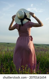 Ein Mädchen auf einem Feld in einem rosa Gingham-Kleid mit weißen Tupfen und einem weißen Sommerhut
