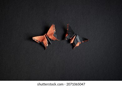 Paar origami oranje en zwarte vlinders op een zwarte textuurachtergrond. Paar geïsoleerde vlinders gecombineerd met tegenovergestelde kleuren op een donkere achtergrond. Ambachtelijke kunst van papier. Wereld origamidag.