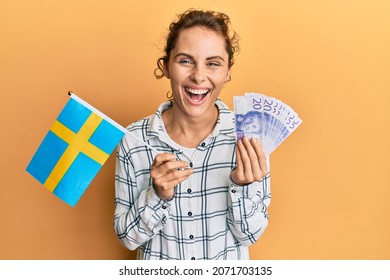 Jonge brunette vrouw met zweden vlag en kroon bankbiljetten glimlachend en hard hardop lachen omdat grappige gekke grap.