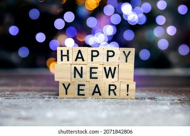 Bright text Happy New Year 2022 on bokeh background written with wooden cubes and snow, colorful festive design, Christmas, New Year, Holiday concept copy space