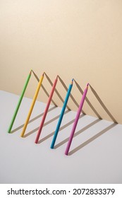Pastel colored crayons in a 3d composition with shadows making triangle shapes.  