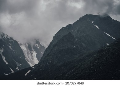 Dunkle, atmosphärische Berglandschaft mit Gletscher auf schwarzen Felsen in bleigrauem, bewölktem Himmel. Schneebedeckte Berge in tiefen Wolken bei Regenwetter. Düstere Landschaft mit schwarzen, felsigen Bergen mit Schnee im Nebel.