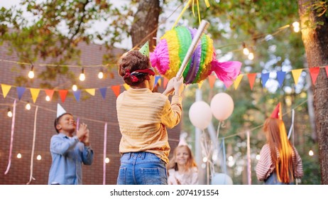 Children celebrating birthday in park. Group of children smash pinata with a bat at birthday party. Children having fun and playing