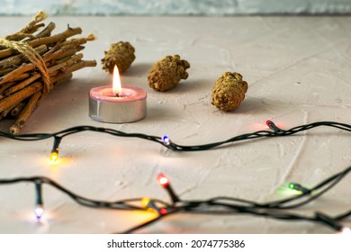 a burning candle pine cones a bundle of brushwood and a Christmas tree garland on a roughly plastered surface. High quality photo