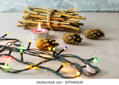 a burning candle pine cones a bundle of brushwood and a Christmas tree garland on a roughly plastered surface. High quality photo
