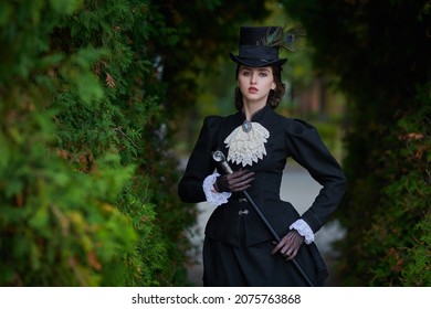 19世紀後半から20世紀初頭の歴史的再建。秋の公園でポーズをとる厳格な黒のドレスを着たエレガントなブルネットの女性。歴史的なメイクと髪型。