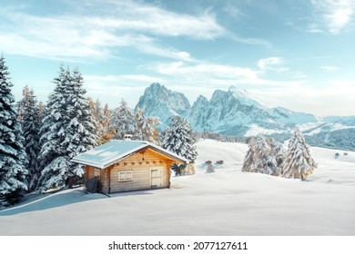 Pintoresco paisaje con una pequeña cabaña de madera en el prado Alpe di Siusi en invierno. Seiser Alm, Dolomitas, Italia. Colinas nevadas con alerce naranja y grupo de montañas Sassolungo y Langkofel