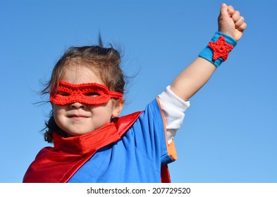 Vajza superhero (femër mosha 04-05 vjeç) e izoluar në sfondin dramatik të qiellit blu me hapësirë ​​kopjimi. foto koncepti i super heroit, fuqia e vajzës, loja e shtirjes, fëmijëria, imagjinata.Njerëz të vërtetë. Hapësira e kopjimit