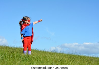 Fëmija (vajzë) superhero në sfondin dramatik të qiellit blu me hapësirë ​​kopjimi. foto koncepti i super heroit, fuqia e vajzës, loja e shtirjes, fëmijëria, imagjinata. Njerëz të vërtetë. Hapësira e kopjimit